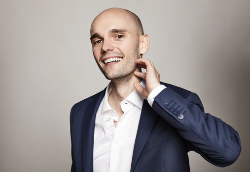 Studio portrait of young cheerful man in blue jacket. He scratches his chin.