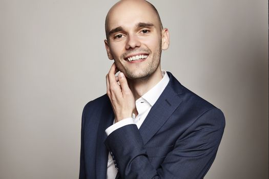 Studio portrait of young cheerful man in blue jacket. He scratches his chin.