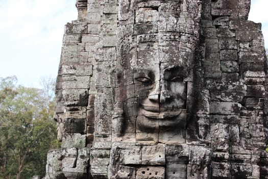 The ruins of a temple in the complex of Angkor, near the ancient city of Siem Reap. Black and gray stones with stone heads and faces, jungle around