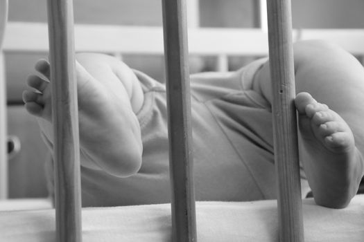 Baby, infant feet sticking out through the rails of a crib, cot, black and white photo, beautiful background for card,  banner, wallpaper design