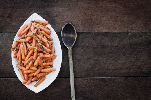 Honey Glazed Baby carrots and old wooden spoon. Image shot from above in flatlay style.