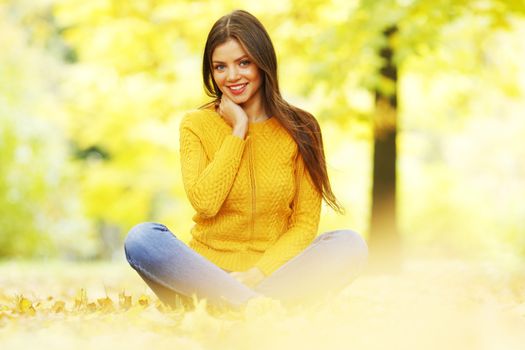 Beautiful woman sitting on autumn leaves in park