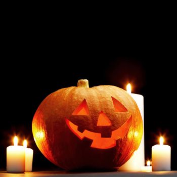 Halloween pumpkin surrounded with candles isolated on black background