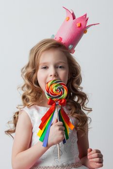 Beautiful little candy princess girl in crown holding big lollipop and smiling