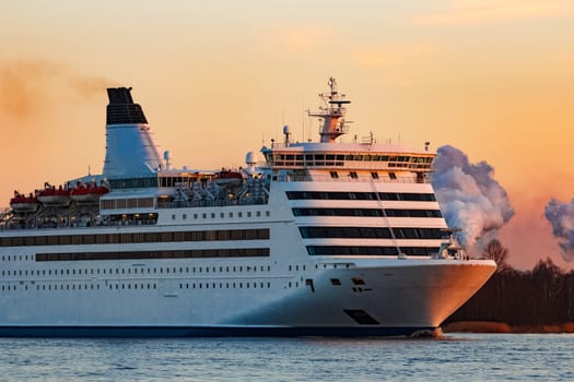 White passenger ship moving against the orange sunset sky