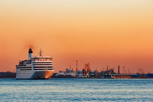 White passenger ship moving against the orange sunset sky