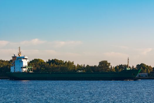 Green cargo ship leaves the port in a clear day