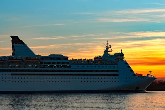 White passenger ship moving against the orange sunset sky