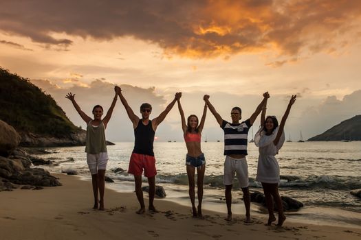 Group of happy people at sea beach at sunset