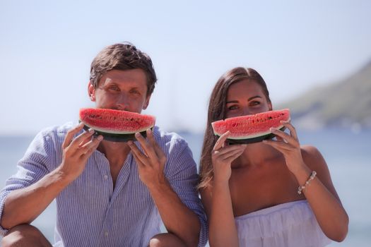 Cheerful couple eating watermelon at sea beach