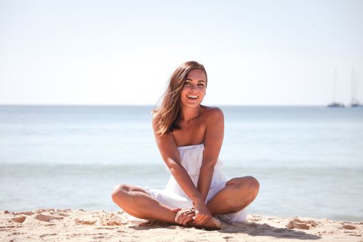 Happy young girl sitting in dress on paradise beach