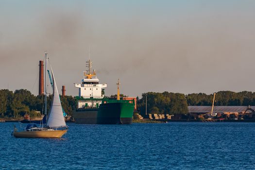 Green cargo ship leaves the port in a clear day