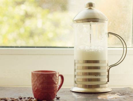 French press with whipped milk on the window