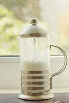 French press with whipped milk on the window