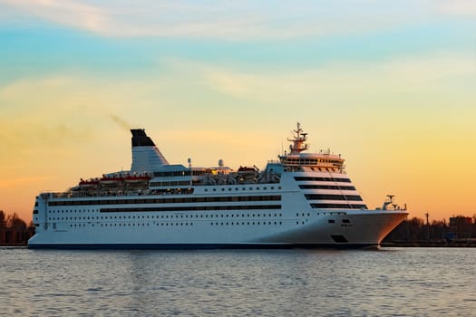White passenger ship moving against the orange sunset sky