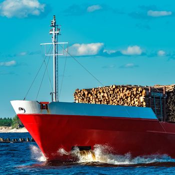 Red cargo ship fully loaded with wood moving at clear day