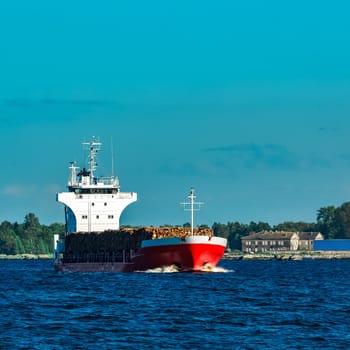 Red cargo ship fully loaded with wood moving at clear day