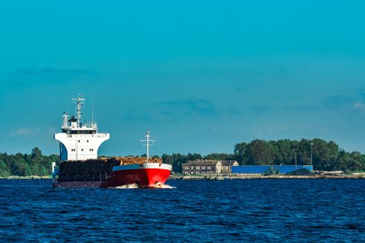 Red cargo ship fully loaded with wood moving at clear day