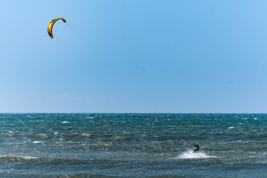 Kitesurfer riding ocean waves on a bright sunny day.