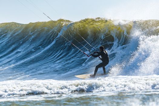 Kitesurfer riding ocean waves on a bright sunny day.