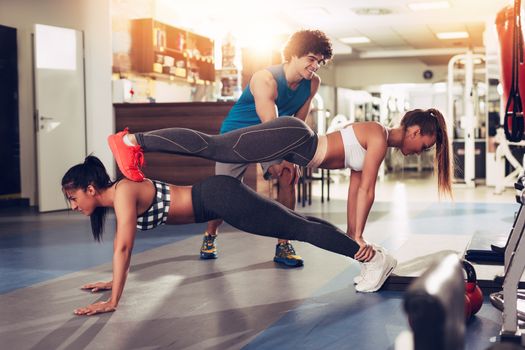 Two smiling girl exercising at the gym with a personal trainer.