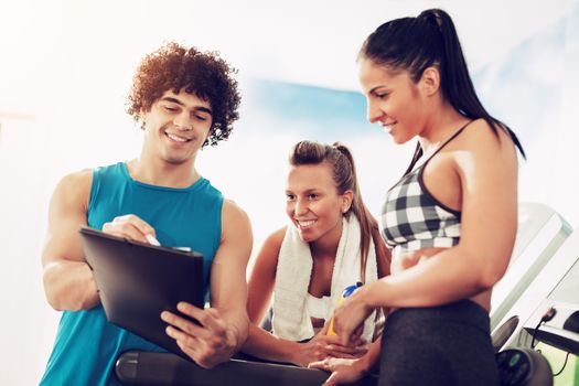 Two happiness female friends consulting with instructor at the gym. 