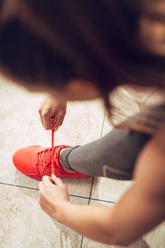 Beautiful girl getting ready for workout at the gym. She is tying shoelace on sneakers. Top view.
