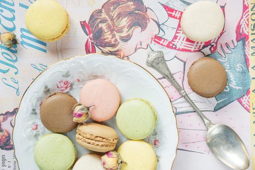 Multicoloured almond cookies (macaroons) on beautiful porcelain plat on vintage magazine; top view, flat lay composition