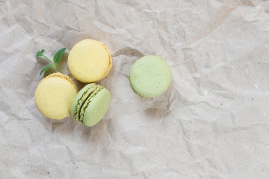 Green and yellow almond cookies (macaroons) and green mint leaves on the background of crumpled craft paper; top view, flat lay composition