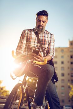 Casual businessman going to work by bicycle. He is sitting on a bike and sending text message.