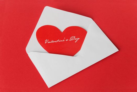 Scarlet heart in a white envelope on the red background