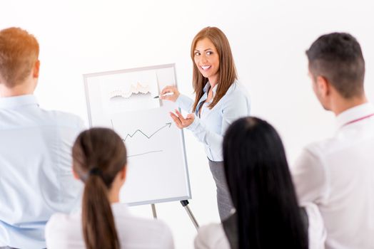 Businesspeople having meeting in a office. Young businesswoman standing  in front of flip chart and having presentation.