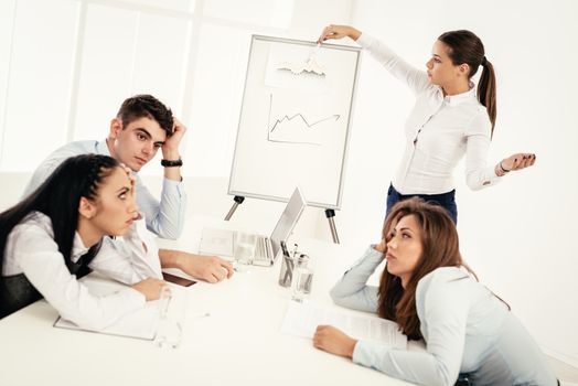 Businesspeople having meeting in a office. Young businesswoman standing  in front of flip chart and having presentation. Her colleagues is booring.