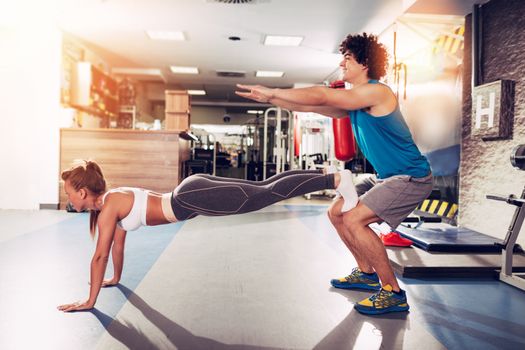 Young muscular couple having workout together at the gym. Handsome boy doing squats exercise, his cute girlfriend doing push-up.