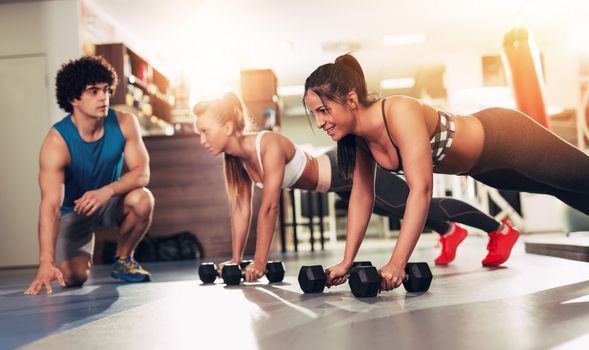 Two smiling girl exercising at the gym with a personal trainer.