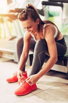 Beautiful girl getting ready for workout at the gym. She is tying shoelace on sneakers.