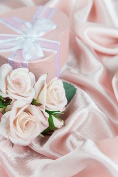 Pink roses and gift box with bow on a background of the silk fabric, vertical image