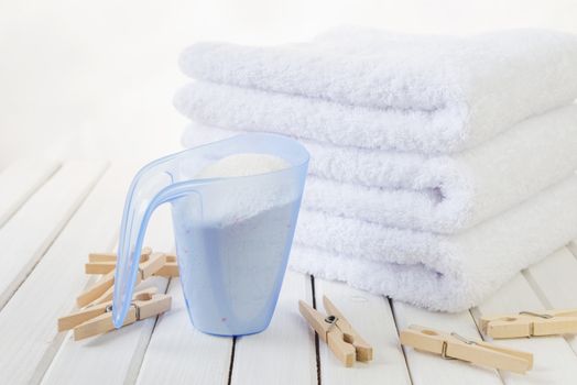 Concept of homework: stack of three white fluffy bath towels, washing powder in measuring cup and wooden clothespins on the background of white boards