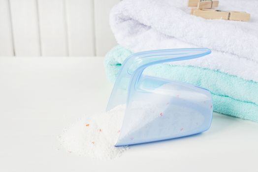 Stack of white and blue fluffy bath towels, washing powder in measuring cup and wooden clothespins on the background of white boards