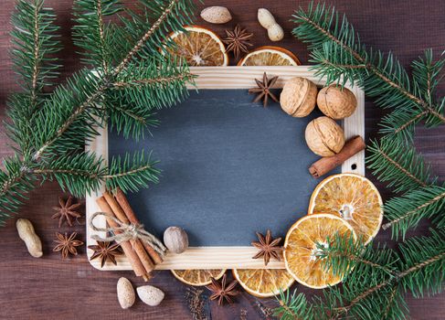 Christmas background: blank chalkboard surrounded by green fir branches and various spices, nuts and dried oranges