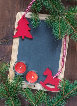 Christmas composition: blank chalkboard surrounded by green fir branches, red rocking horse and spruce and two burning candles