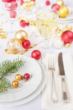 Silver knife and fork, christmas ball and green spruce branche lie on the white porcelain plate, glass of white wine, which is located on a table covered with a white tablecloth
