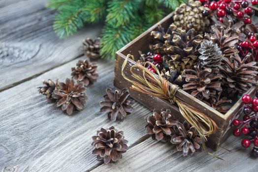 Christmas concept: full wooden box of pine cones and red holly berries and spruce branches on the background of old unpainted wooden boards