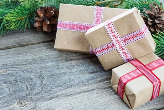 Christmas composition of pine cones, spruce branches and stack of gift boxes on the background of old unpainted wooden boards; with copy-space