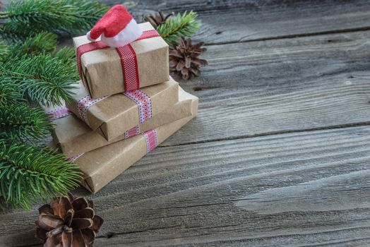 Christmas composition of pine cones, spruce branches and stack of gift boxes with Santa's cap on the background of old unpainted wooden boards; with copy-space