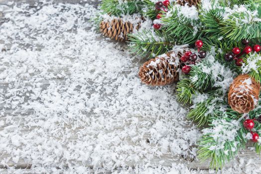 Christmas frame composed of green  branches of spruce, pine cones and holly berries on the background of wooden boards, covered with white snow flakes. Flat lay composition for greeting cards, websites, social media, magazines,  bloggers, artists etc.