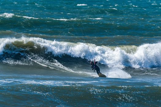 Kitesurfer riding ocean waves on a bright sunny day.