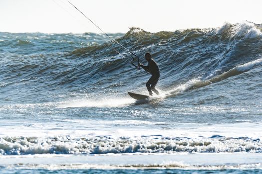 Kitesurfer riding ocean waves on a bright sunny day.