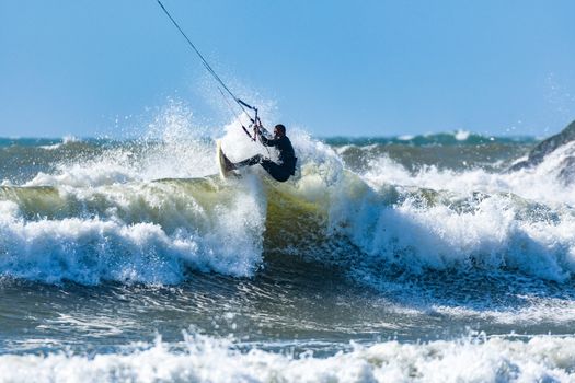 Kitesurfer riding ocean waves on a bright sunny day.