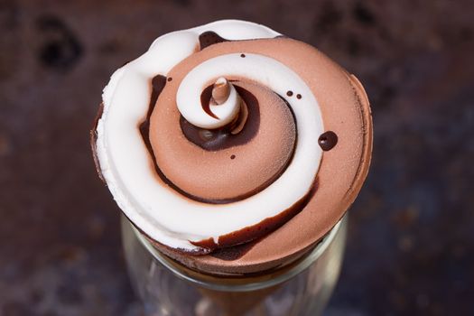 Ice cream in waffle cone with chocolate syrup toppingn in glass on dark black background